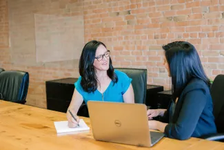 woman in teal t-shirt sitting beside woman in suit jacket by Amy Hirschi courtesy of Unsplash.